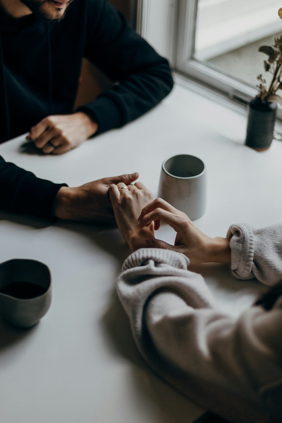 Two people holding hands across a table, a cup of coffee between them